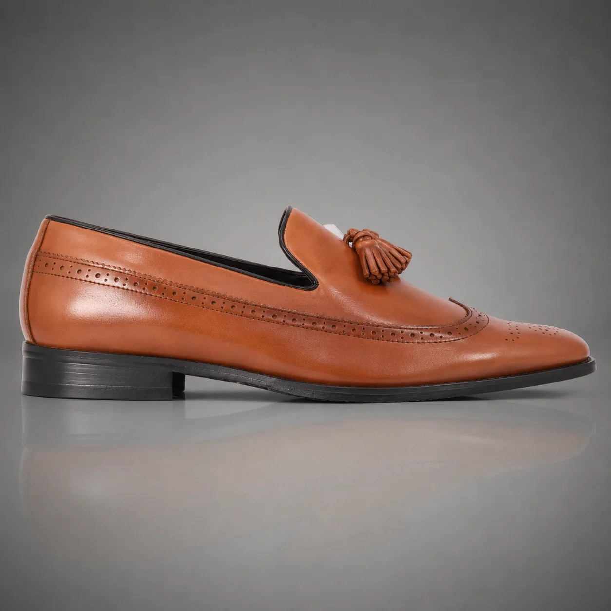 A single men's brown leather John Drake tassel loafer with brogue detailing, shown in a side profile against a gray gradient background.
