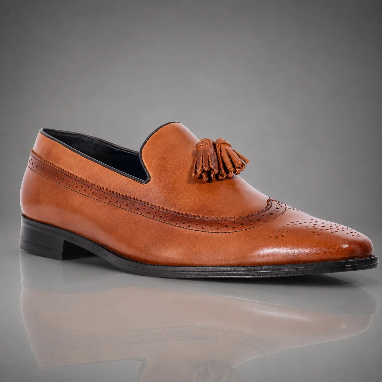 A single men's brown leather John Drake tassel loafer with brogue detailing, shown in a side profile against a gray gradient background.