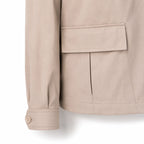 Close-up of a beige jacket sleeve and pocket, showing fabric texture and button cuff detail against a white background.