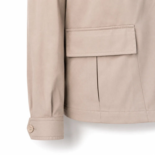 Close-up of a beige jacket sleeve and pocket, showing fabric texture and button cuff detail against a white background.
