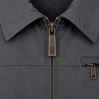 Close-up of a dark grey Durburg Mistral collared jacket with an antique bronze zipper pull featuring an engraved script 'D' logo, and a matching zippered chest pocket.