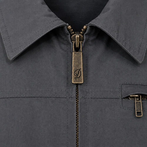 Close-up of a dark grey Durburg Mistral collared jacket with an antique bronze zipper pull featuring an engraved script 'D' logo, and a matching zippered chest pocket.