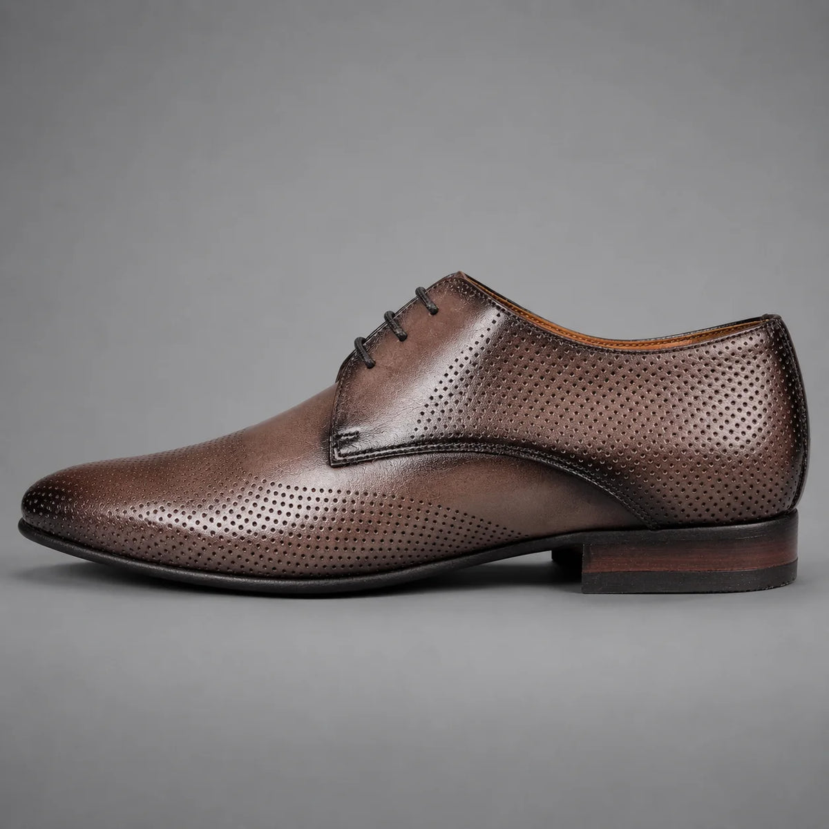 A single brown leather oxford dress shoe with perforated detailing, shown in a side profile against a neutral gray background.