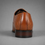A single brown leather dress shoe shown from the rear, featuring a textured argyle pattern on the quarter and a dark brown stacked heel, set against a solid gray background.