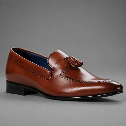 A single brown leather tassel loafer shoe with brogue detailing and a low black heel, photographed on a neutral gray background.