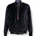 A black velvet bomber jacket displayed on a dark mannequin torso against a white background. The jacket features a silver zipper with a pink 'NAVADA' tag, side pockets, and a small metal 'NAVADA' logo badge near the bottom hem.