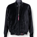 A black velvet bomber jacket displayed on a dark mannequin torso against a white background. The jacket features a silver zipper with a pink 'NAVADA' tag, side pockets, and a small metal 'NAVADA' logo badge near the bottom hem.