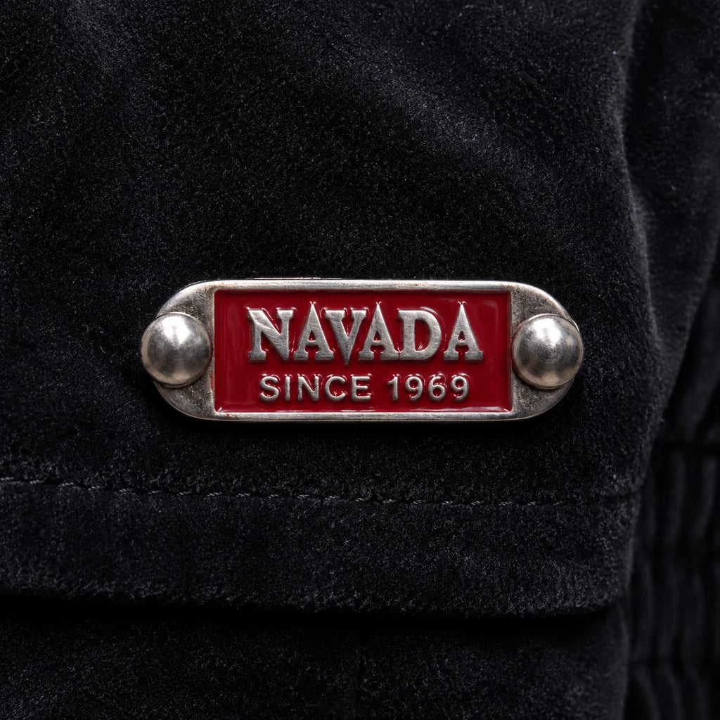 A close-up of a black textured garment featuring a silver-tone metal lapel pin with a red enamel background and the text 'NAVADA SINCE 1969'.