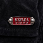 A close-up of a black textured garment featuring a silver-tone metal lapel pin with a red enamel background and the text 'NAVADA SINCE 1969'.